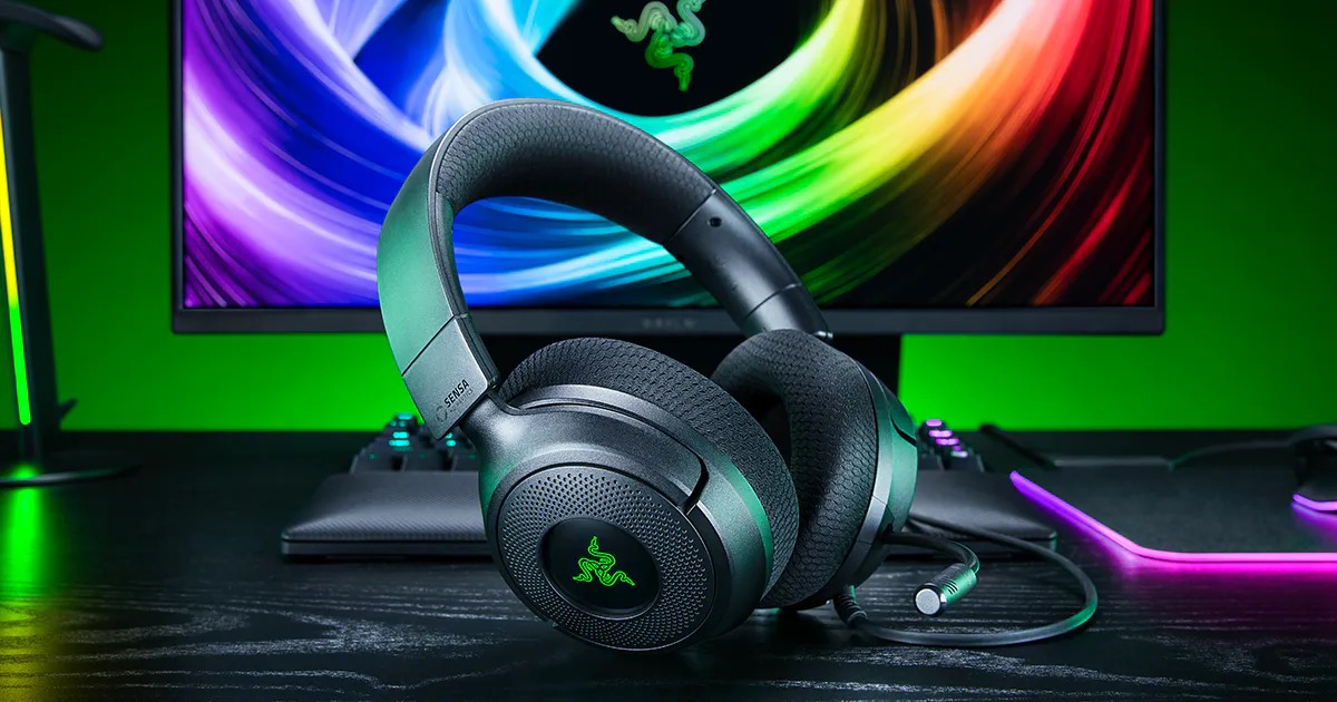モニターの前の机に置かれた、黒いRazer Kraken V4 X Sensa HD Haptics。イヤーカップの中央にRazerのロゴが緑色に光っている。