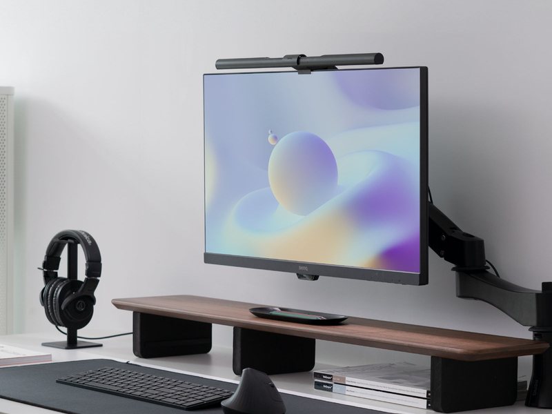 白い机の上のモニターの上の縁に、黒い棒状のモニターライトが掛かっている。机の上にはキーボード、マウス、ヘッドホンだけが置かれ、デスクライトは無い。