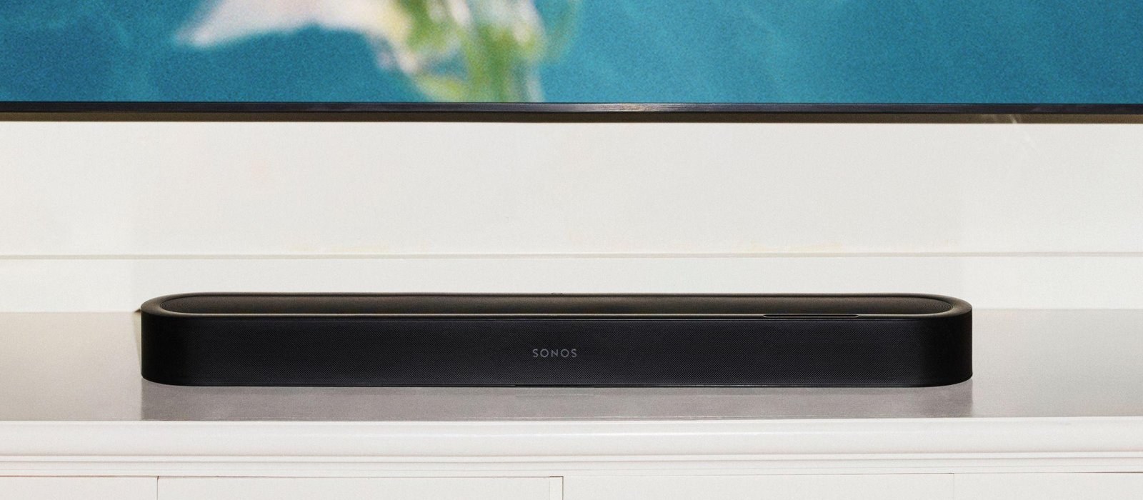 白いテレビ台に置いた黒いSonos Beam Ultraを正面から写した写真。上にテレビの画面の下端が見え、本体の中央にSONOSのロゴがある。