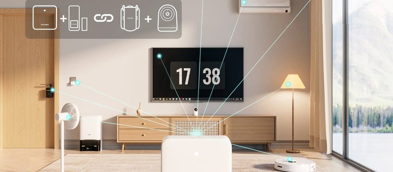 リビングの床に置いたSwitchBotのハブから、エアコン、テレビ、照明、扇風機、ロボット掃除機、玄関のロックへ線が伸びている写真。左上にハブと他の機器をつなぐアイコンがある。